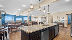 A spacious kitchen with a central island, modern pendant lighting, and a view through large windows.