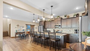 A modern kitchen with wooden flooring, stainless steel appliances, and a bar area with stools.