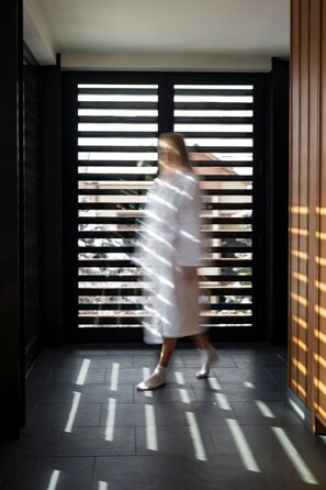 A person walking in a hallway with a modern design, featuring a dark floor and a window with horizontal blinds. - LARCH HOUSE (Whitefish)