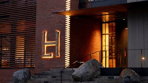 A modern building with a brick facade, large windows, and a prominent illuminated 'H' sign. - LARCH HOUSE (Whitefish)
