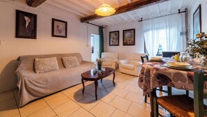 Ein gemütliches Wohnzimmer mit Sofa, Sesseln, einem Couchtisch und einem Esstisch für zwei Personen.