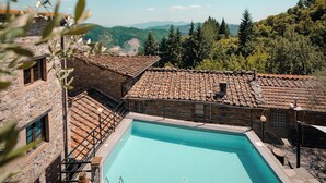Ein Pool, umgeben von Steingebäuden mit Terrakotta-Dächern, mit Blick auf eine gebirgige Landschaft.