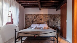 Ein Schlafzimmer mit Steinswand, einem Bett mit Metallgestell, einem Nachttisch und einem Fenster mit Vorhängen.
