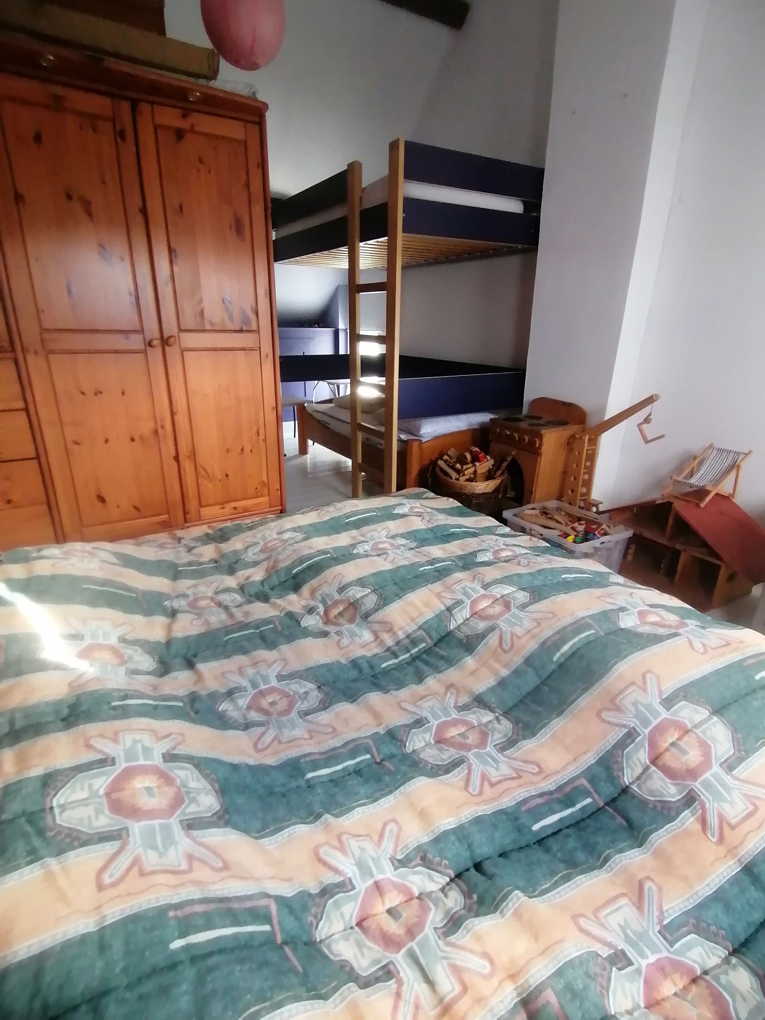 Een kamer met stapelbedden, een houten garderobe, een bed met een decoratief sprei en een stoel.