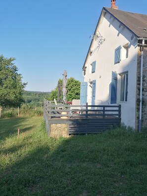 Ein weißes Gebäude mit blauen Fensterläden, einer Holzterrasse und einer Steinmauer.