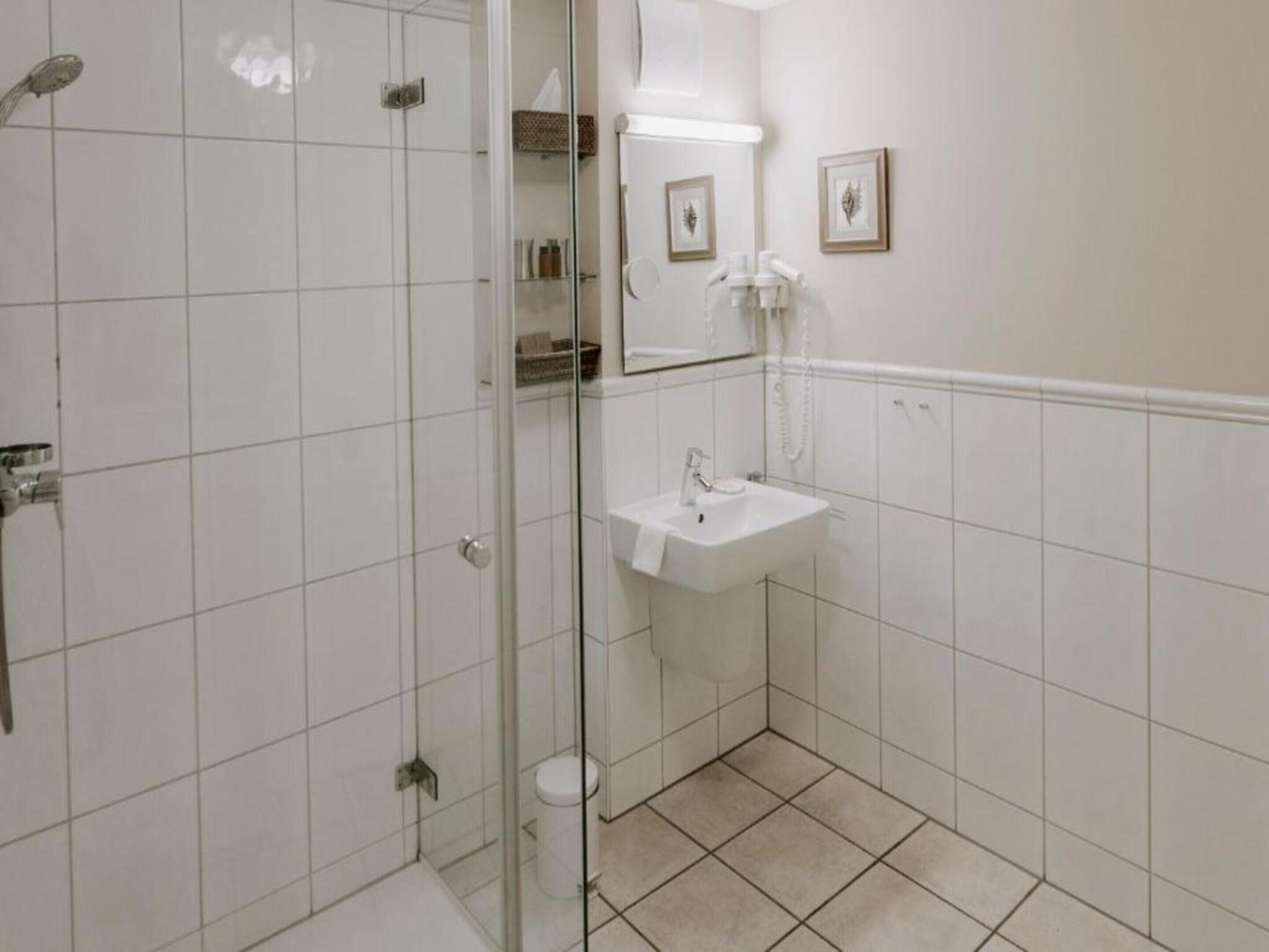 A bathroom with a glass shower enclosure, a sink, and a mirror.