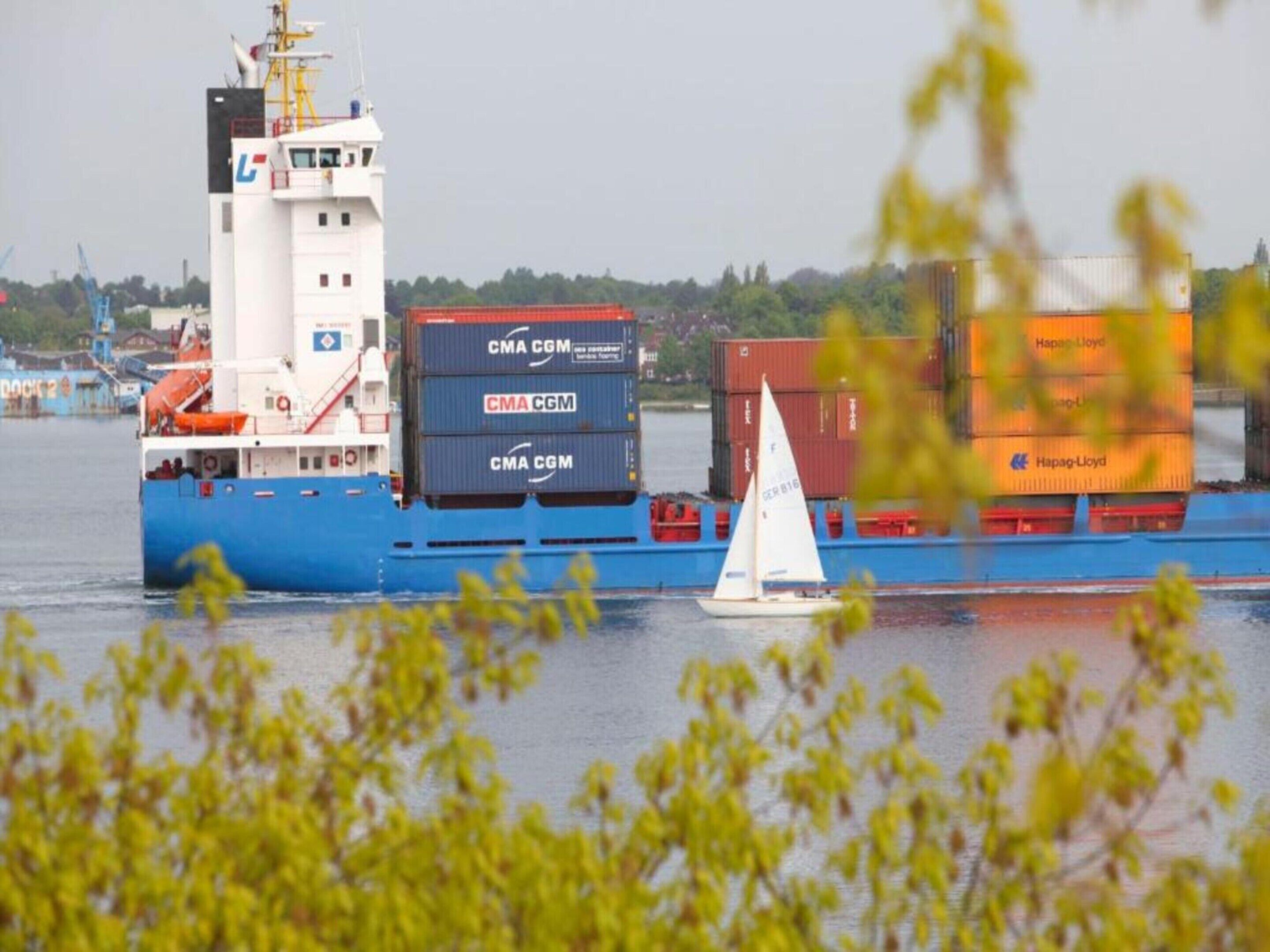 A cargo ship with stacked containers labeled 'CMA CGM' and a sailboat in the foreground.