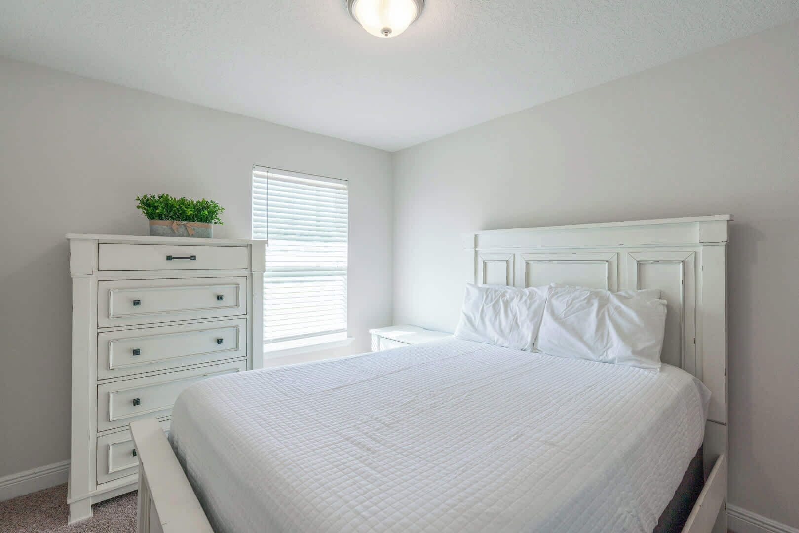 A bedroom with a bed, a dresser, a nightstand, and a window with blinds.