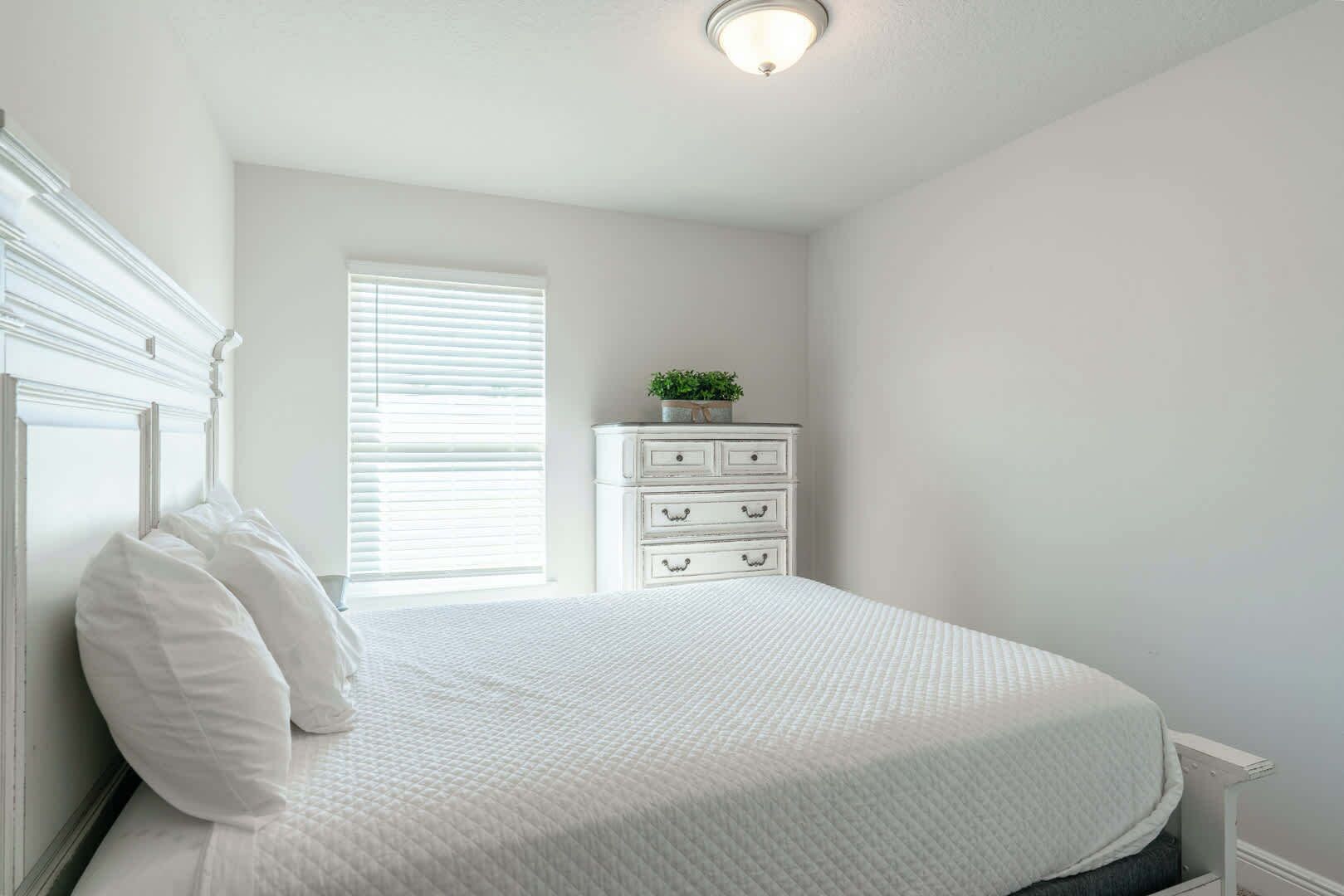 A bedroom with a bed, white dresser, and a window with blinds.