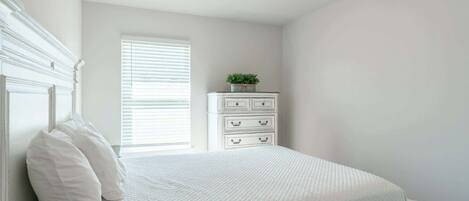 A bedroom with a bed, white dresser, and a window with blinds.