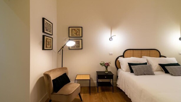 A bedroom with a bed, a chair, a bedside table with a lamp, and framed pictures on the wall. - Relais Virgilio  (Rome)