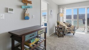 A living room with a wooden console table, a chair, a lamp, and a view of the lake. - Sunset Serenity - Lakeside Pool & Location! (Osage Beach)