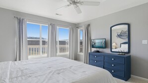 A bedroom with a bed, a dresser, a television, and a large window with curtains. - Sunset Serenity - Lakeside Pool & Location! (Osage Beach)