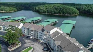 A hotel with a parking lot, a green-roofed building, and a body of water with boats. - Sunset Serenity - Lakeside Pool & Location! (Osage Beach)