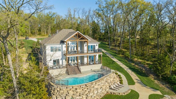 A two-story house with a stone retaining wall, a swimming pool, and a deck. - Luxe Manor - Heated Lakefront Pool, Lily Pad & More! (Sunrise Beach)