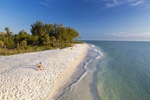 A sandy beach with clear turquoise water, a few people, and dense greenery along the shoreline. - Cape Haven - Heated Pool, Ping Pong & More! (Cape Coral)