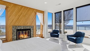 A bedroom with a fireplace, large windows, and a view of the outdoors.