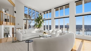 A spacious living room with large windows, a white sofa, a coffee table, and a potted plant.