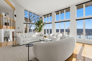 A spacious living room with large windows, a white sofa, a coffee table, and a potted plant. - Vantage Point - Heated Pool, Hot Tub, & Views! (Sunrise Beach)