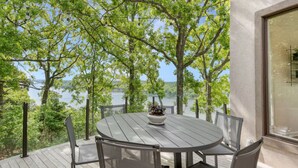 A round table with chairs on an outdoor deck, overlooking a body of water with trees.