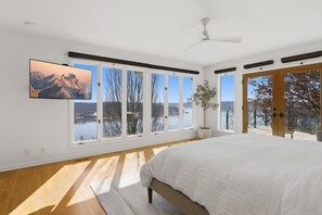 A bedroom with a large bed, multiple windows, a ceiling fan, and a TV on the wall. - Vantage Point - Heated Pool, Hot Tub, & Views! (Sunrise Beach)