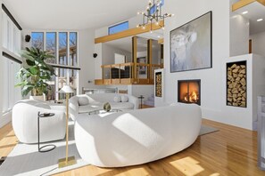 A modern living room with a white sofa, a glass coffee table, a fireplace, and a large abstract painting. - Vantage Point - Heated Pool, Hot Tub, & Views! (Sunrise Beach)