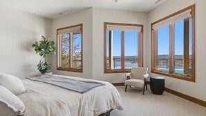 Un dormitorio con cama, una silla, una planta y ventanas amplias con vistas.