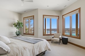 A bedroom with a bed, a chair, a plant, and large windows with a view.