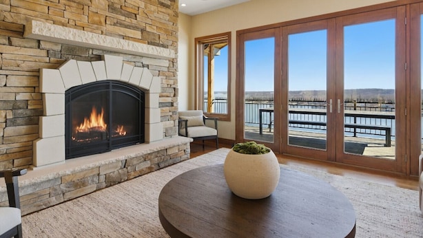 Una chimenea con pared de piedra, una mesa redonda con una planta y vista a un muelle a través de grandes puertas de vidrio.