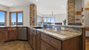 Una cocina con encimeras de granito, armarios de madera, una pared decorativa de piedra y vistas amplias a través de grandes ventanales.