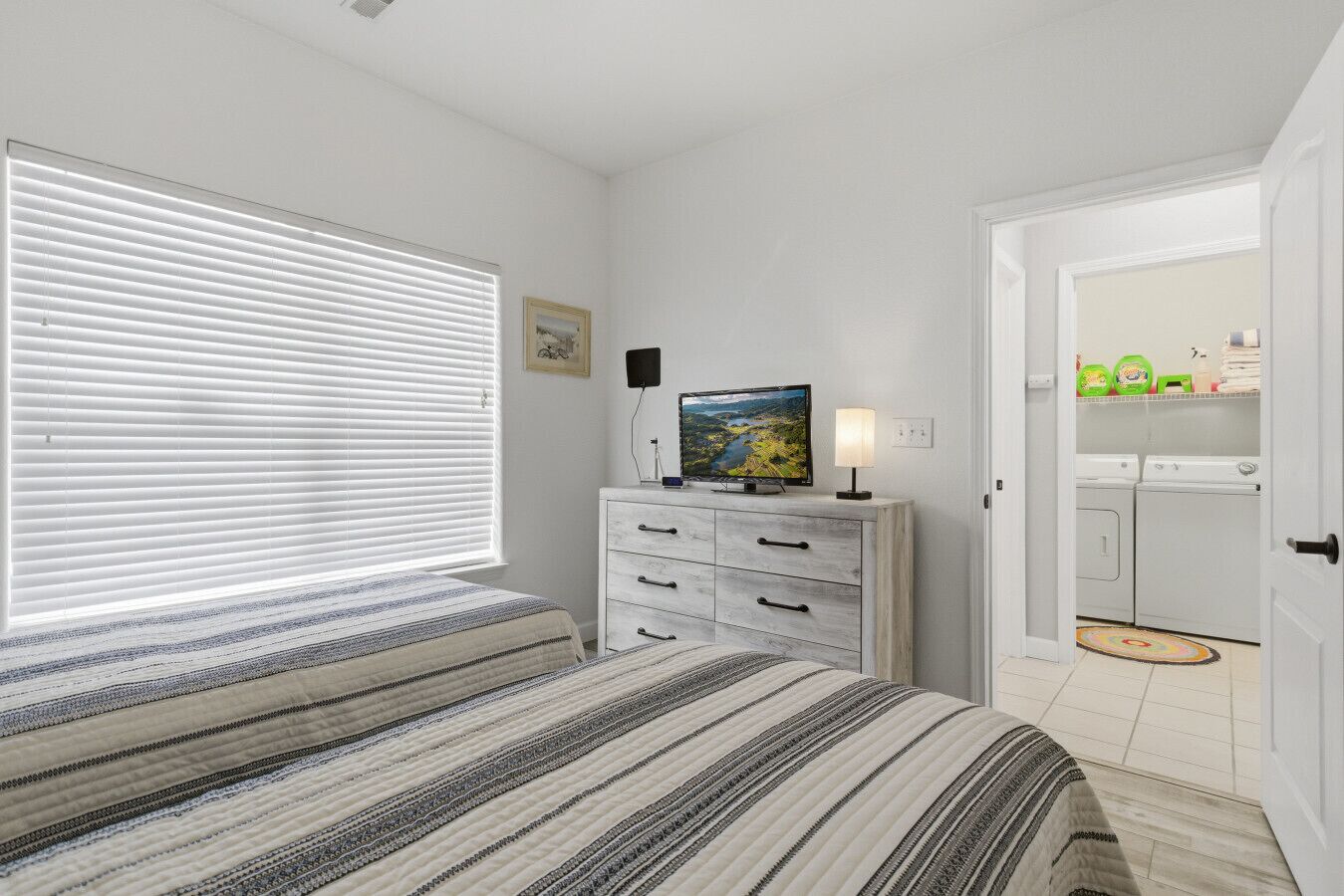A bedroom with a bed, a dresser, a television, and a door leading to a laundry area.