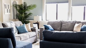 Ein Wohnzimmer mit einem grauen Sofa, einem blauen Sessel und einem kleinen Tisch mit einer Lampe.