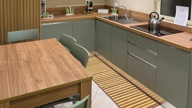 A compact kitchen with a wooden dining table, green chairs, a built-in oven, and a window with a view.