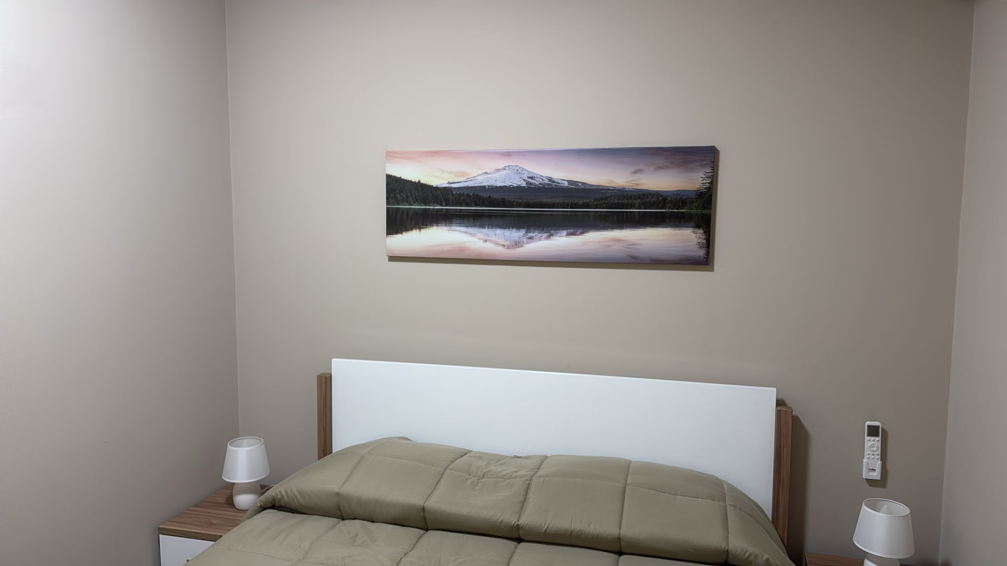 Una camera da letto con un letto, un comodino, una lampada da comodino, una lampada a parete e un dipinto di un paesaggio montano.