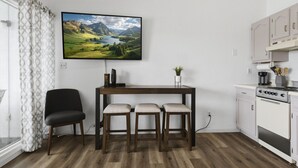 A modern kitchen with a wooden table, bar stools, a TV mounted on the wall, and a window with patterned curtains. - Lakeview for Two - Lakeside Pool & Top Floor! (Osage Beach)