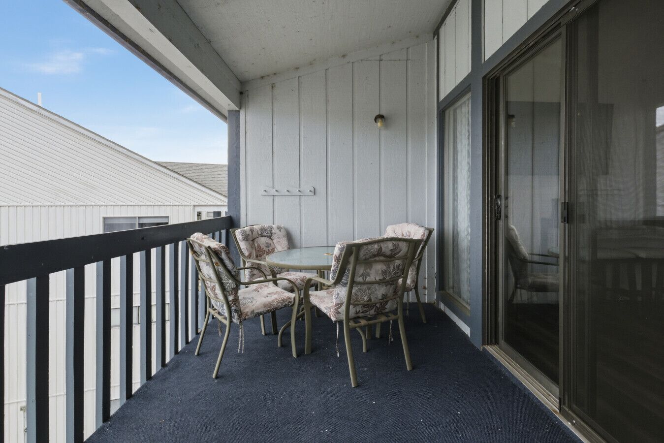 A balcony with a round table and four chairs, a sliding glass door, and a view of the sky.