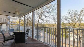 A covered outdoor area with a table and chairs, a ceiling fan, and a view of trees and buildings.