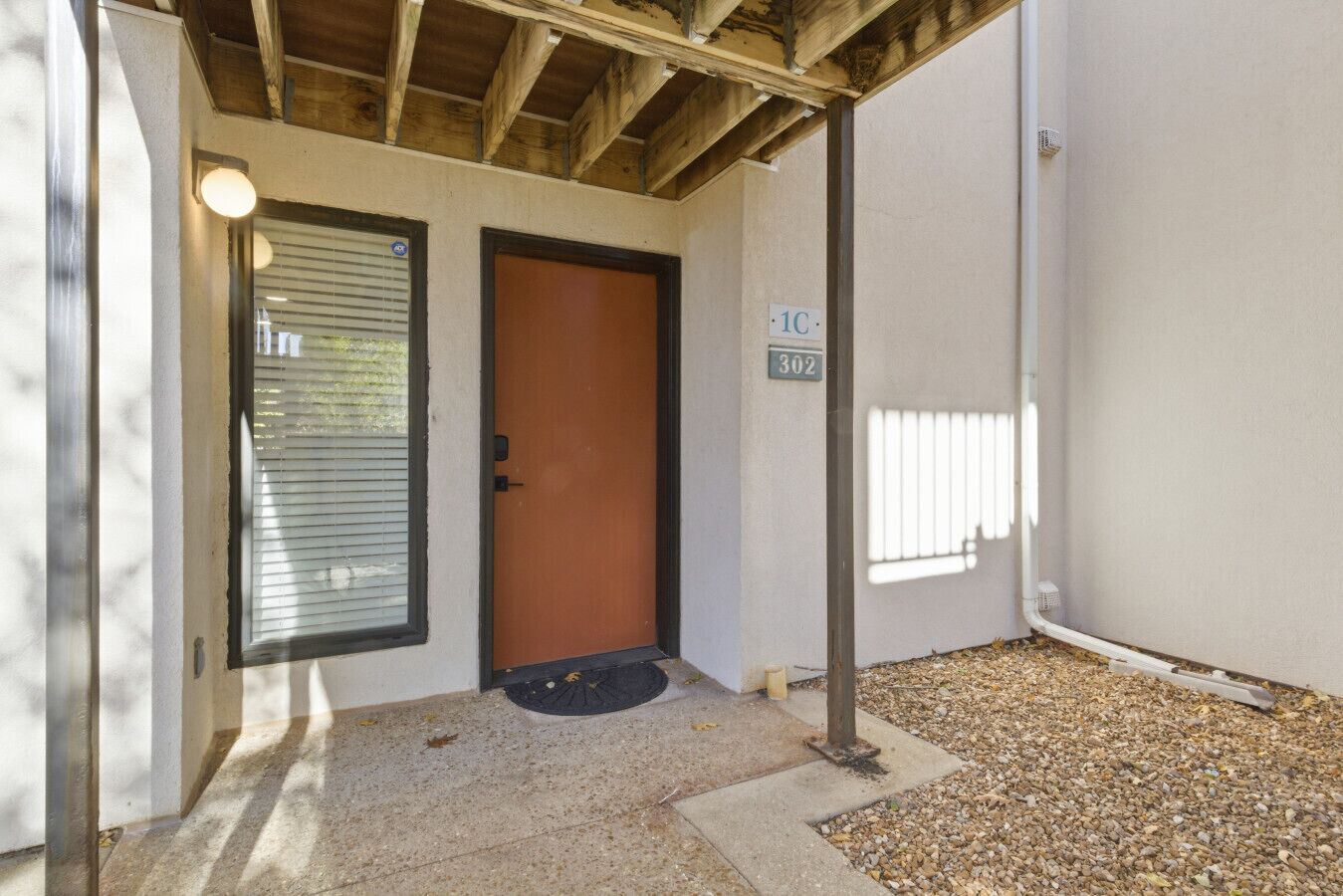 A building entrance with a door, a window with blinds, a number sign, and a small porch area.