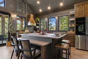 A modern kitchen with a large island, bar stools, and a stainless steel refrigerator.