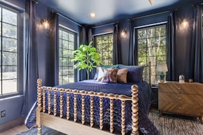 A bedroom with a large bed, dark walls, and multiple windows.