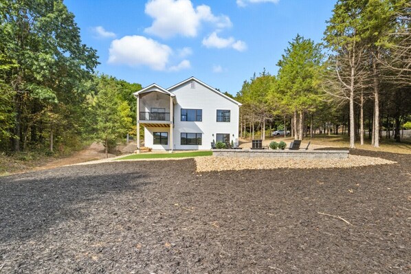 A two-story house with a balcony, surrounded by trees and a gravel driveway.