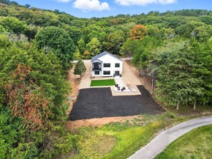 A modern house with a small patio area, surrounded by dense forest.