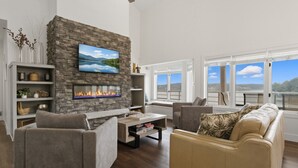 Een woonkamer met een stenen openhaard, een flatscreen-tv en een groot raam met uitzicht op een prachtig panorama.