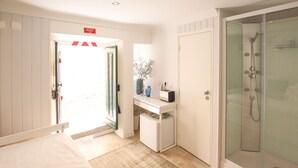 A hotel room with a bed, a desk with a vase, a shower, and a door marked 'Emergency Exit.' - Nomad s Castel Lisbon - The Solo (Lisbon)
