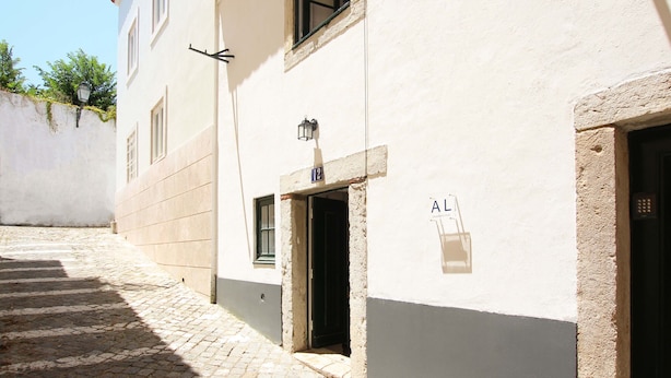 A narrow cobblestone alley with a building featuring a door marked with the number 12, a small window, and a sign with the letters 'AL' on the wall. - Nomad s Castel Lisbon - The Solo (Lisbon)