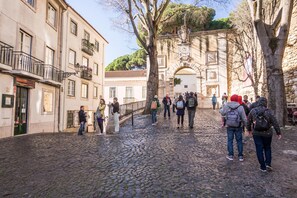 A cobblestone street with historic buildings, a stone archway, and people walking. - Nomad s Castel Lisbon - The Solo (Lisbon)