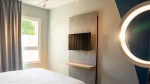 A hotel room with a bed, a mounted TV, a bedside table, and a window with curtains. - Ibis Budget Compiègne Centre-Ville (Compiegne)
