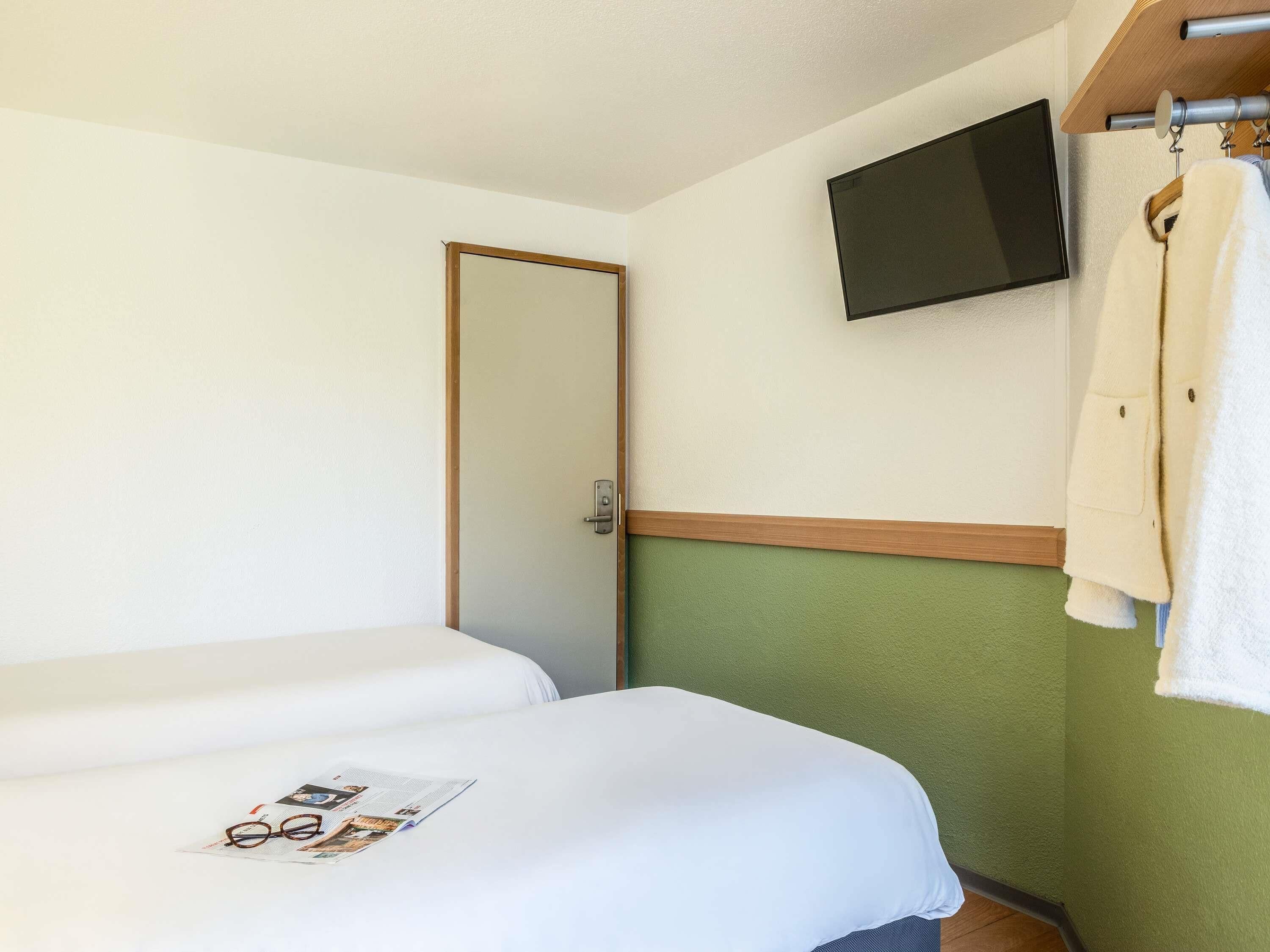 A hotel room with a bed, a television mounted on the wall, and a coat hanging on a rack.