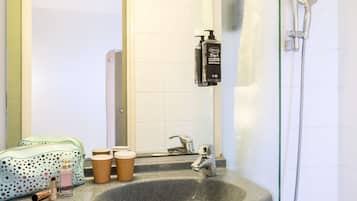 Une salle de bain avec un lavabo en granit, une douchette à main, un miroir et un sac vert à pois.