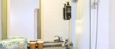 Un baño con lavamanos de granito, ducha de mano, espejo y una bolsa verde con lunares.